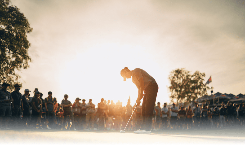 多くの観客の前で夕日を背に冷静にパットを打つゴルファー